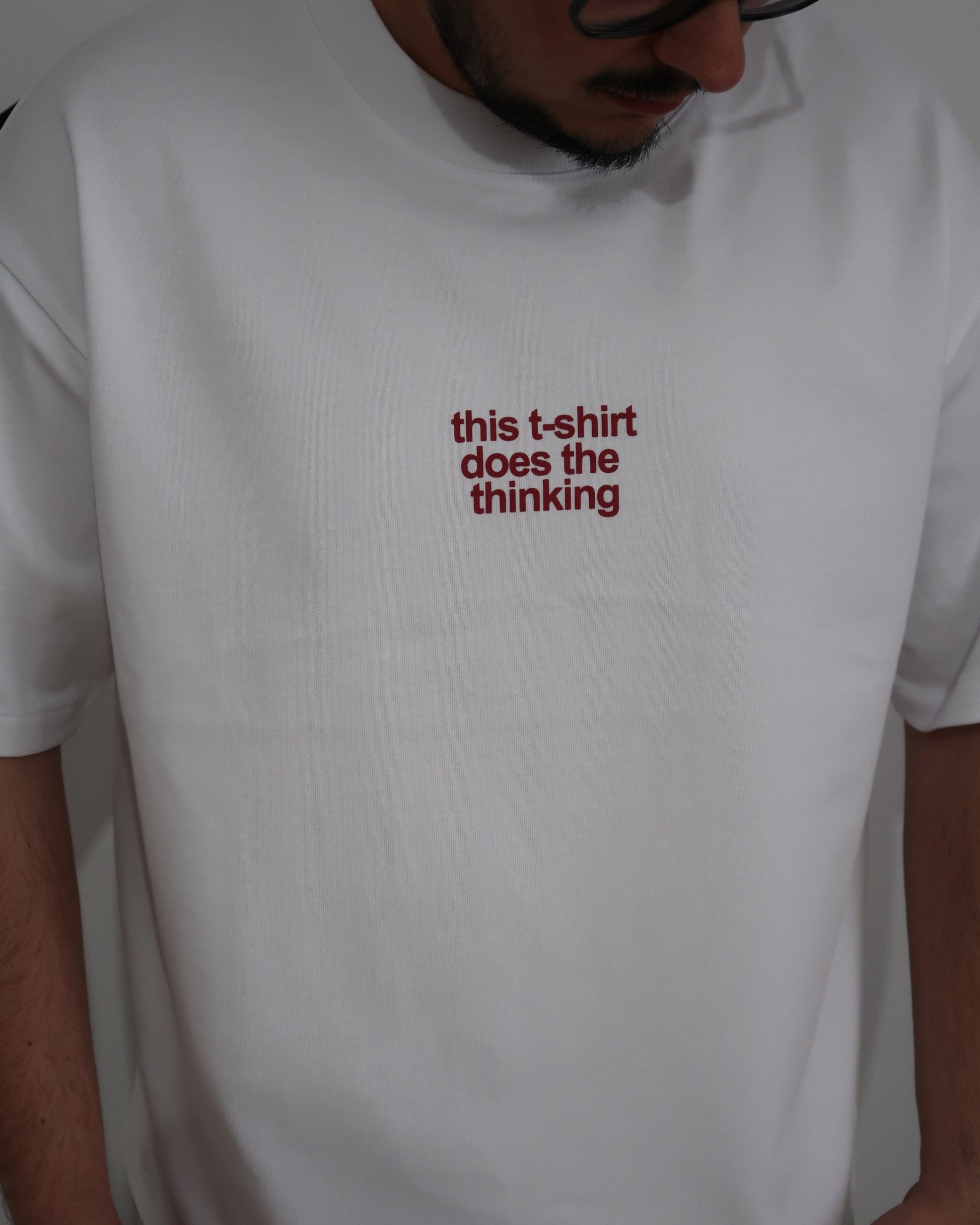 White t-shirt with red text 'this t-shirt does the thinking' worn by a person.